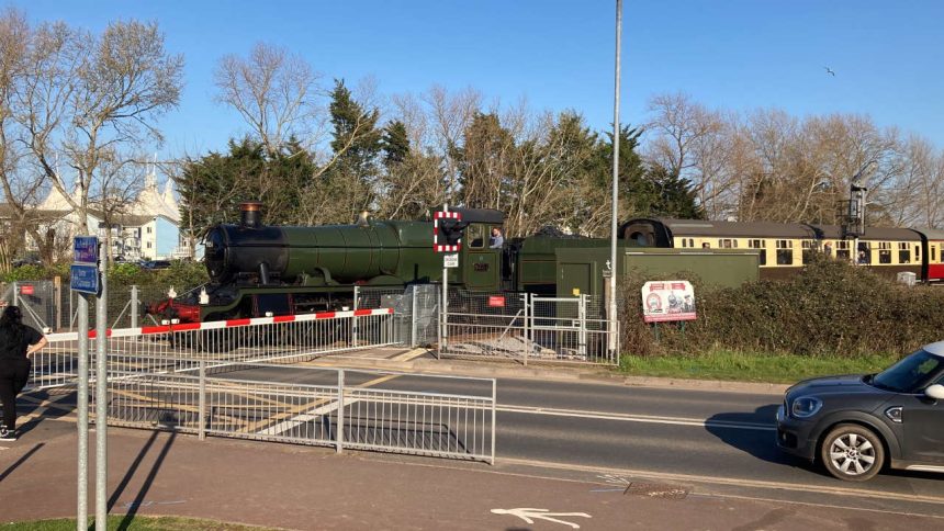 traffic waits as the first West Somerset Railway passenger-carrying train in more than two years steams towards Minehead station over the modernised Seaward Way level crossing