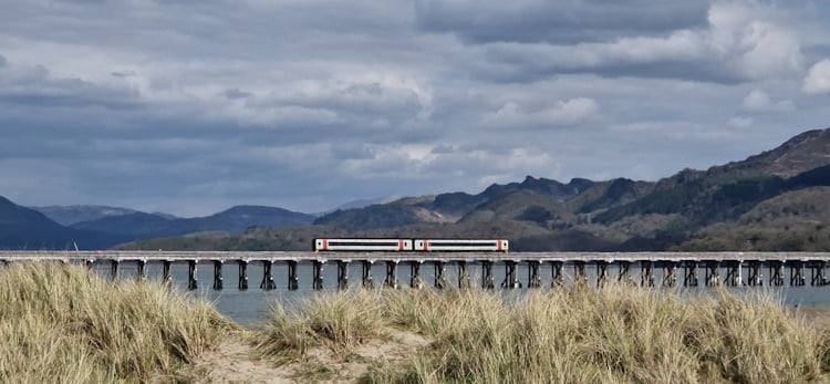 TfW Class 158 crossing Barmouth Bridge, with the hills and mountains of Snowdonia in the background.