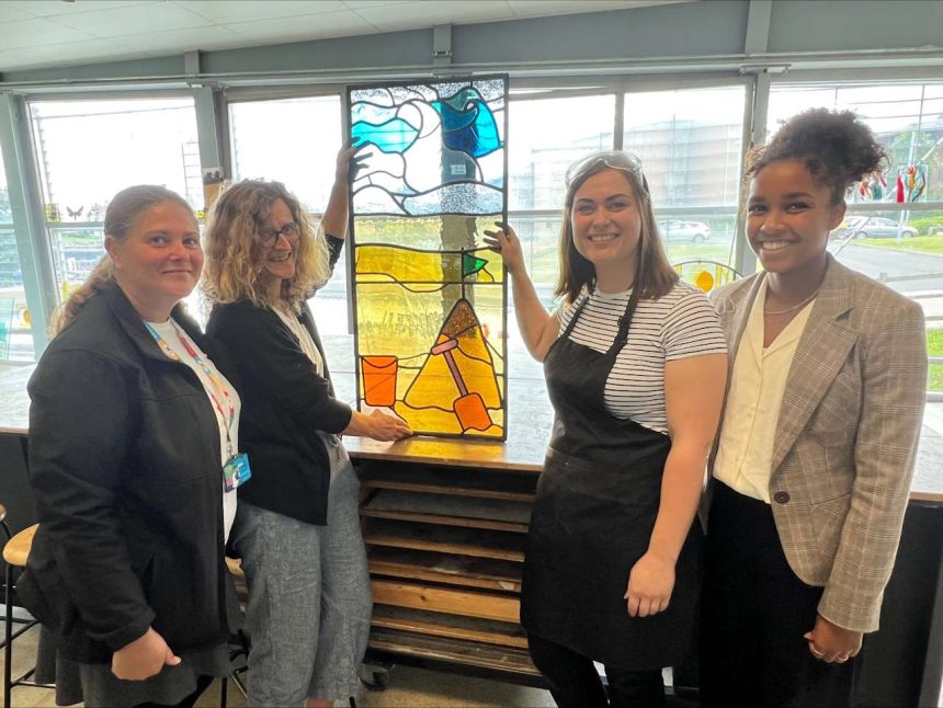 same of the Nexus team with the stained-glass makers at the Sunderland National Glass Centre, holding the stained glass art work from Monkseaton Metro station.