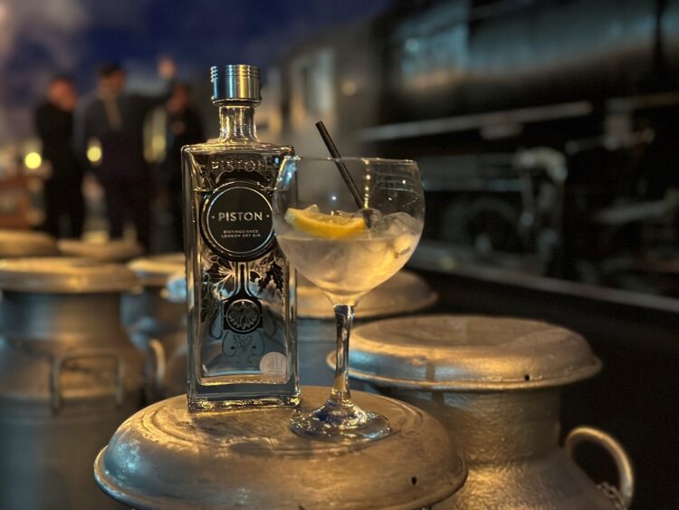 A bottle of Gin sits on top of a milk churn with a black steam locomotive just out of focus in the bacjground.